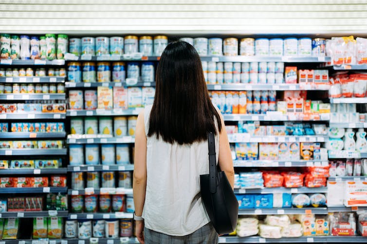 A woman stands in front of a massive grocery store display of infant formula.