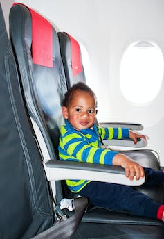 excited toddler sits in an airplane window seat